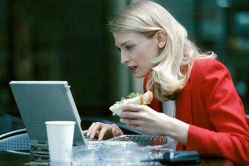 Business woman works on laptop computer while eating lunch.