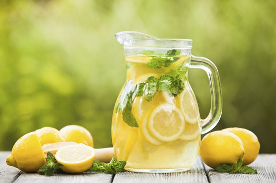 Preparation of the lemonade drink. Lemonade in the jug and lemons with mint on the table outdoor